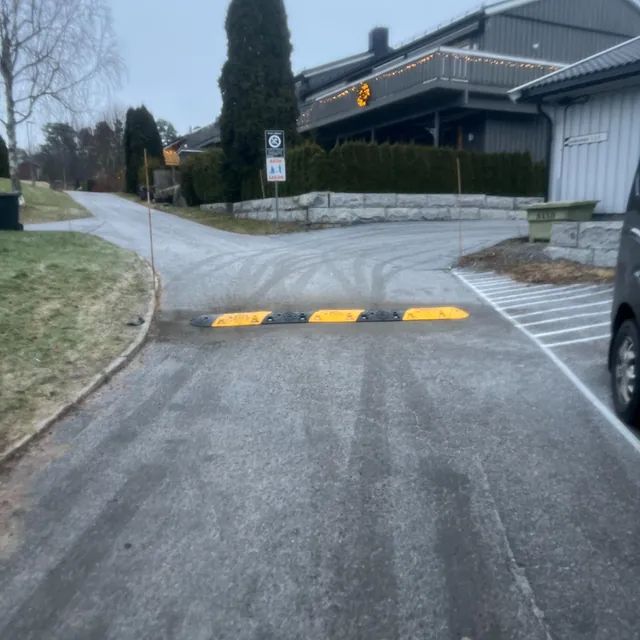 Veibump i gul og svart plast midt på asfaltert vei ved boligområde med juledekorasjoner.