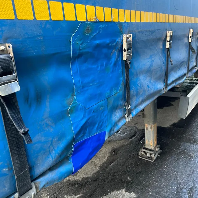 Blå presenning på lastebil reparert med lapp etter utskjæring, festet med stropper og låser.