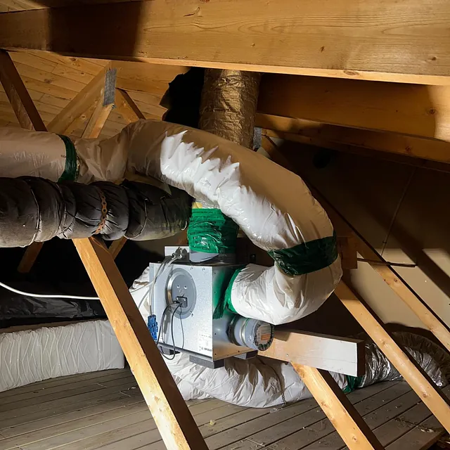 Ventilasjonsanlegg med isolerte rør installert på loft med synlige trebjelker og skråtak.
