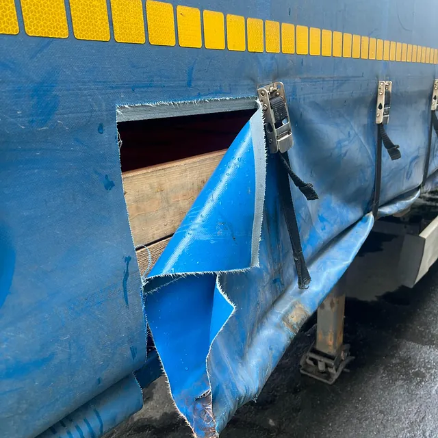 Utskåret hull i blå presenning på lastebil avslører last, med gule refleksmerker over.