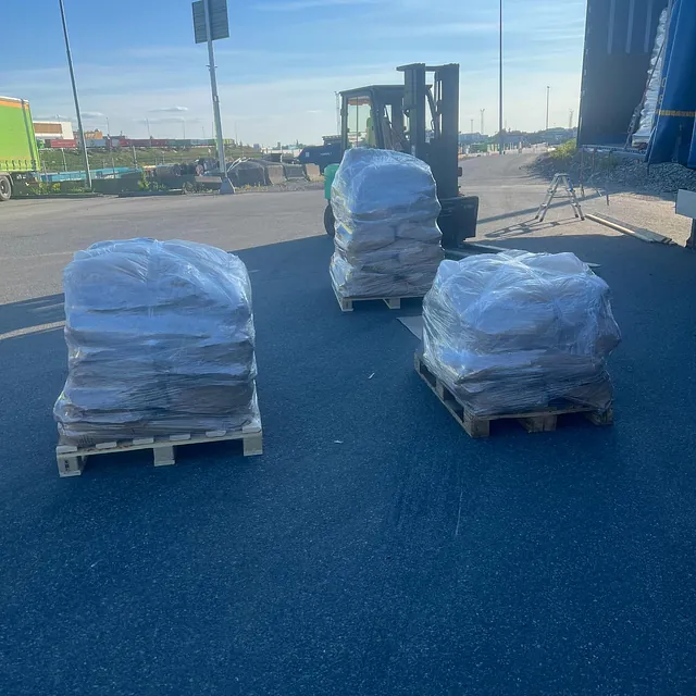 Tre plastinnpakkede paller står klare for lasting ved lastebil og truck på industriområde.